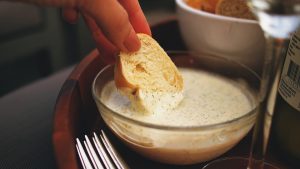 Schale mit cremigem Knoblauchdip und Brot auf einem Tisch