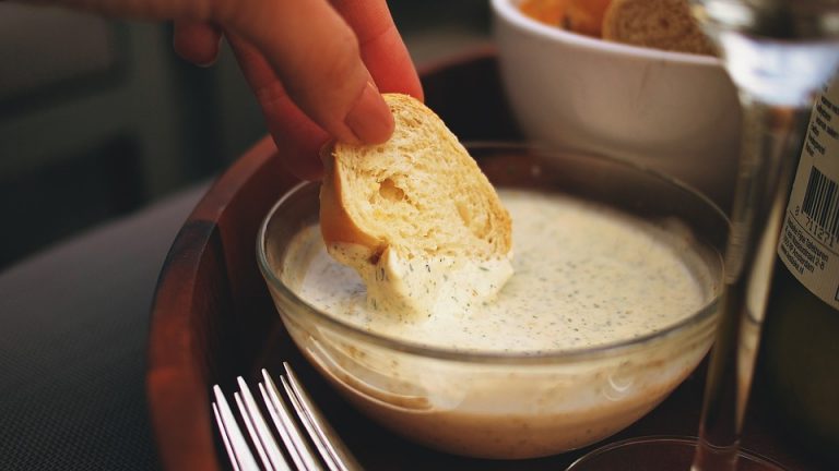 Schale mit cremigem Knoblauchdip und Brot auf einem Tisch
