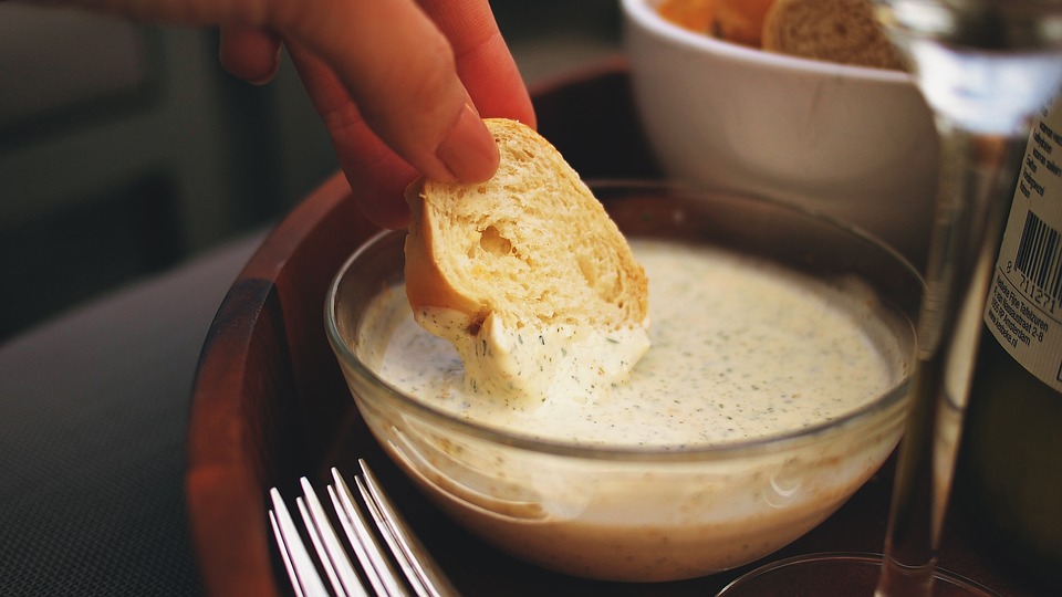 Schale mit cremigem Knoblauchdip und Brot auf einem Tisch