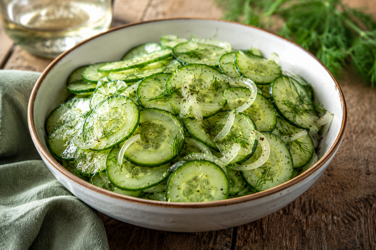 Schale mit schwedischem Gurkensalat, Gurkenscheiben, Dill und Zwiebeln auf Holztisch